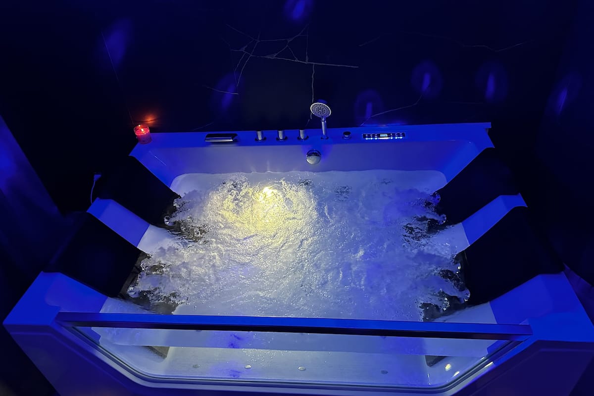 A hot tub with water jets, a control panel, and a ceiling light.