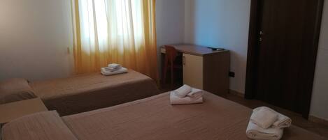 A hotel room with two single beds, a desk, a chair, and a TV mounted on the wall.