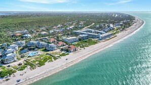 Vista aérea de un complejo turístico frente al mar, con villas en la playa, una piscina y una extensión de arena.