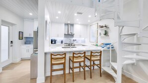 Una cocina moderna con armarios blancos, una isla central con taburetes de bar y una escalera con barandillas blancas.