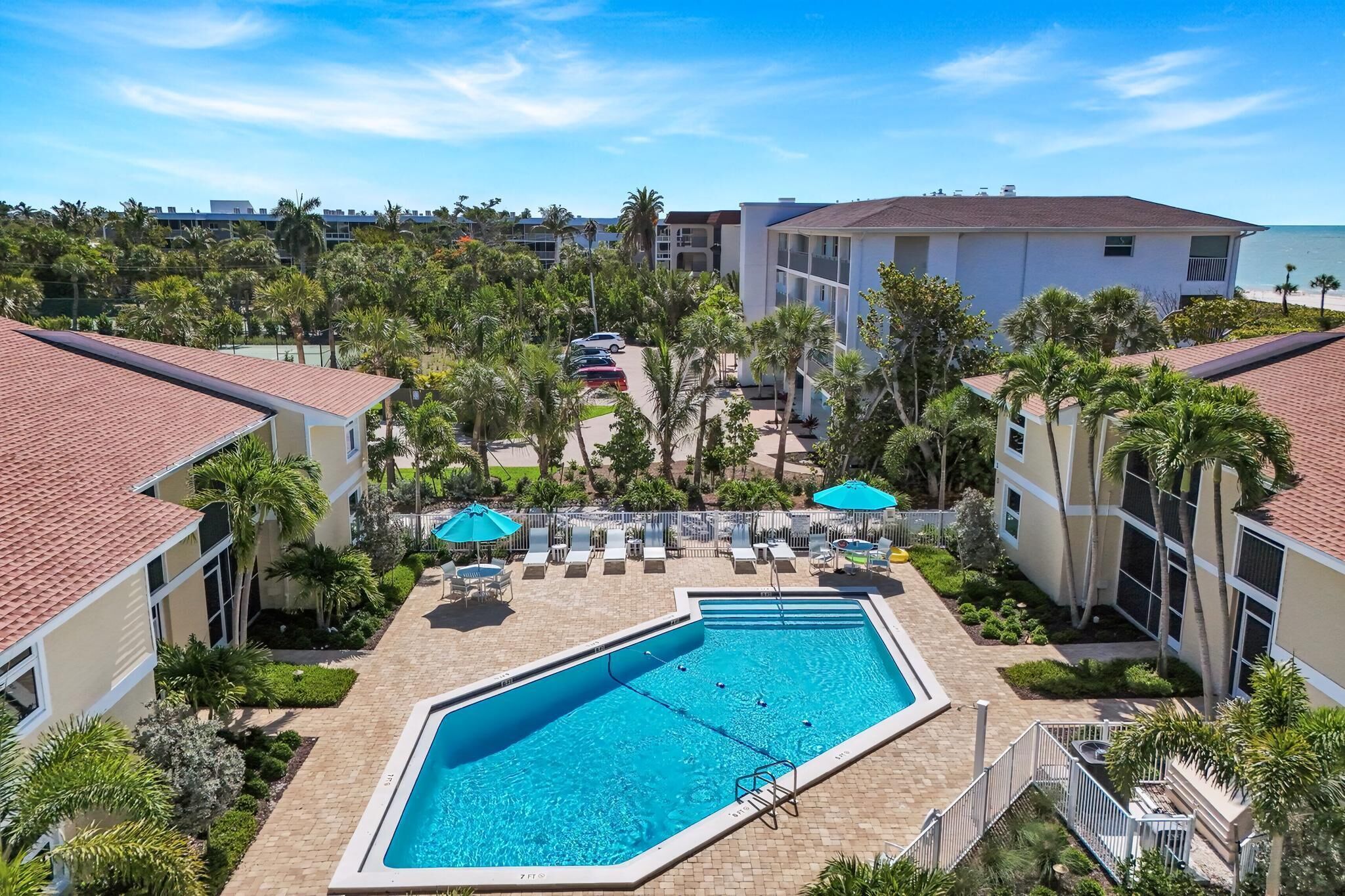 A swimming pool surrounded by lounge chairs and umbrellas, with palm trees and a clear blue sky.