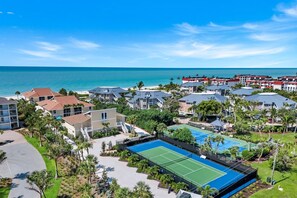 Un complejo turístico en la costa con varias edificaciones, una cancha de tenis y vista al océano.