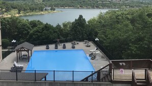 En swimmingpool med solstolar och en pergola, omgiven av ett staket och träd.