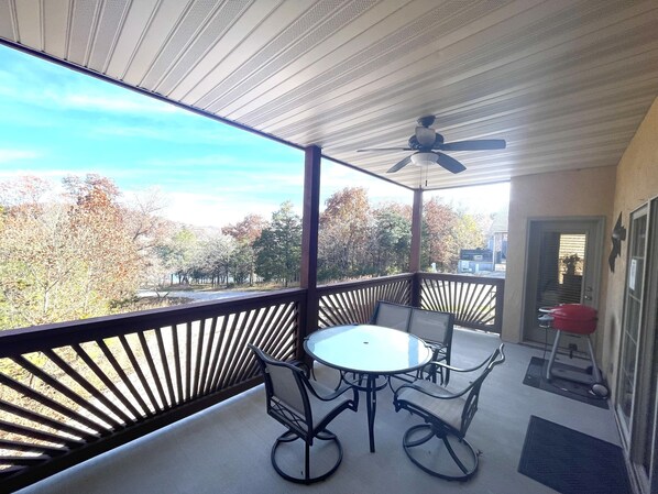 A covered balcony with a table and chairs, a ceiling fan, and a view of trees and a building in the background. - INDIAN POINT CONDO WITH PRIVATE BOAT SLIP. EASY ACCESS. NO STAIRS (Branson)