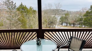 Un balcone con un tavolo in vetro e due sedie, con vista su un lago e alberi.
