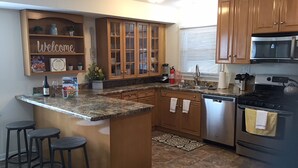 A kitchen with wooden cabinets, granite countertops, a built-in island with stools, stainless steel appliances, and a welcome sign. - Modern! Professionally Cleaned, Self Check In - Sleeps 10 (Kenosha)