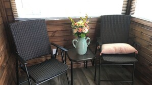 Two wicker chairs with cushions, a small table with a vase of flowers, and wooden walls with a window in the background. - Modern! Professionally Cleaned, Self Check In - Sleeps 10 (Kenosha)
