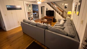 Una sala de estar con un sofá gris, una mesita de centro, un televisor y una escalera que lleva a otra habitación.