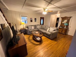 A living room with a sectional sofa, a coffee table, a ceiling fan, a wooden floor, and a wooden dresser with a mirror. - Welcome to your home away from home! (Beattyville)