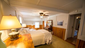 Una habitación de hotel con cama, escritorio, lámpara, ventilador de techo y puerta que da a otra habitación.