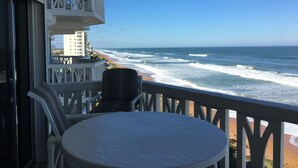 Een balkon met uitzicht op de oceaan en het strand, met een ronde tafel en stoelen.