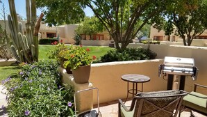 An outdoor patio with a grill, seating, and potted plants.