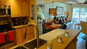 A modern kitchen with stainless steel appliances, a central island with glasses, and a dining area with a sofa and table.