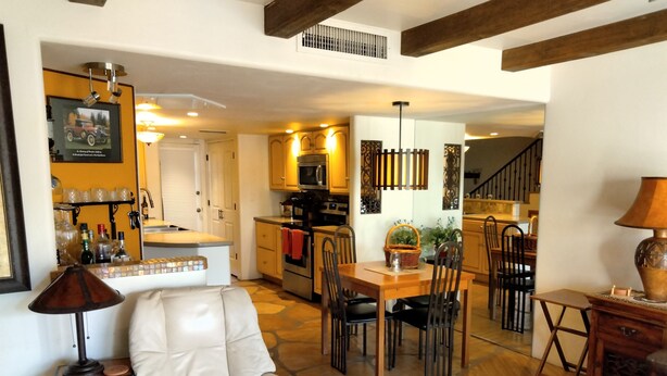 A spacious living area with a leather armchair, dining table, and chairs, a kitchen with modern appliances, and a staircase leading to another level.