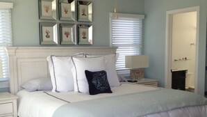 Une chambre avec un lit blanc, un ventilateur de plafond et des œuvres d’art encadrées accrochées au mur.