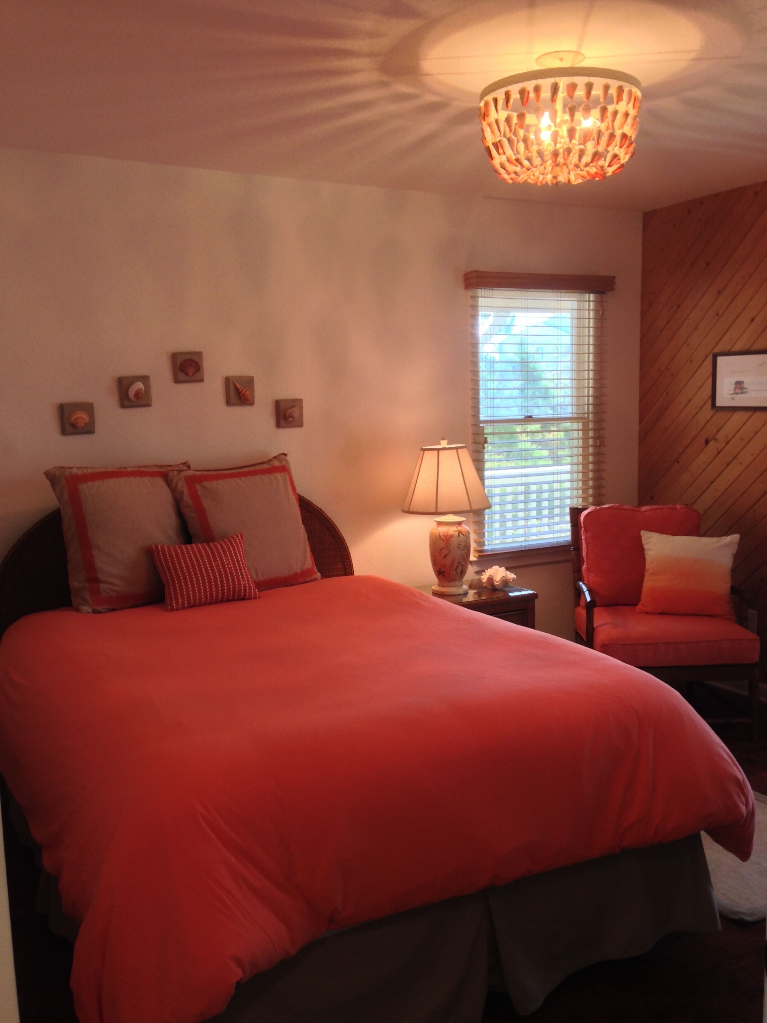 A bedroom with a large bed, a chair, a lamp, and a chandelier.