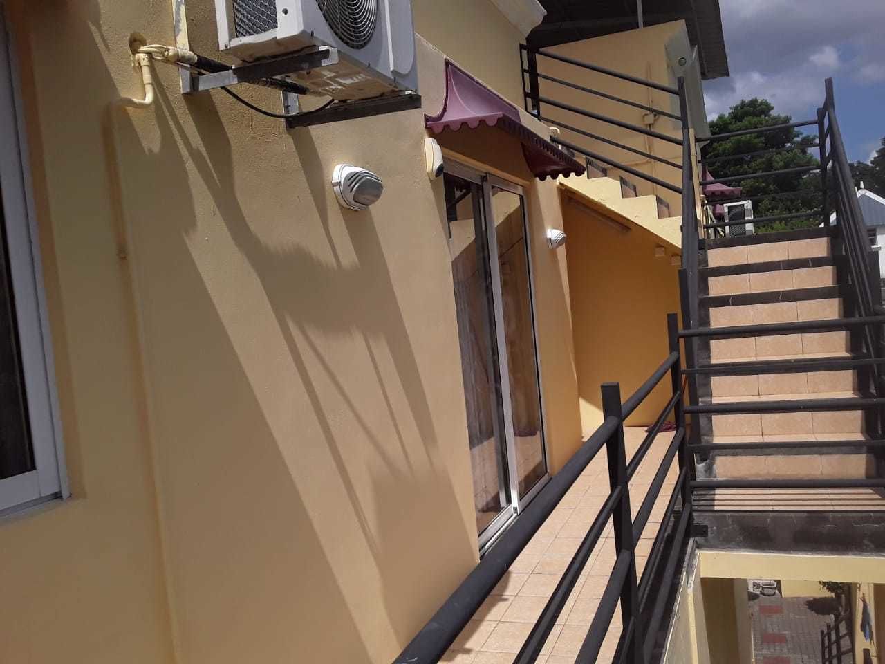 Un bâtiment à la façade jaune, un escalier avec des rampes noires et une fenêtre équipée d’un appareil de climatisation.