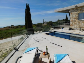 A private pool area with a stone wall, lounge chairs, and a table with a bottle and fruit.