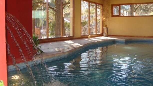 An indoor swimming pool with large windows, wooden beams, and a stone wall. - L'Hirondelle - Adults Only (La Falda)