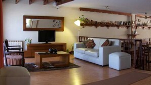 A living room with a wooden ceiling, a television, a sofa, a coffee table, and a dining area with a chandelier. - L'Hirondelle - Adults Only (La Falda)