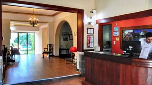 A hotel reception area with a wooden reception desk, a chandelier, and a view of the outdoor seating area. - L'Hirondelle - Adults Only (La Falda)