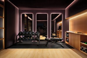 A modern gym with a mirrored wall, a rack of dumbbells, a bench, and a wooden cabinet with shelves.