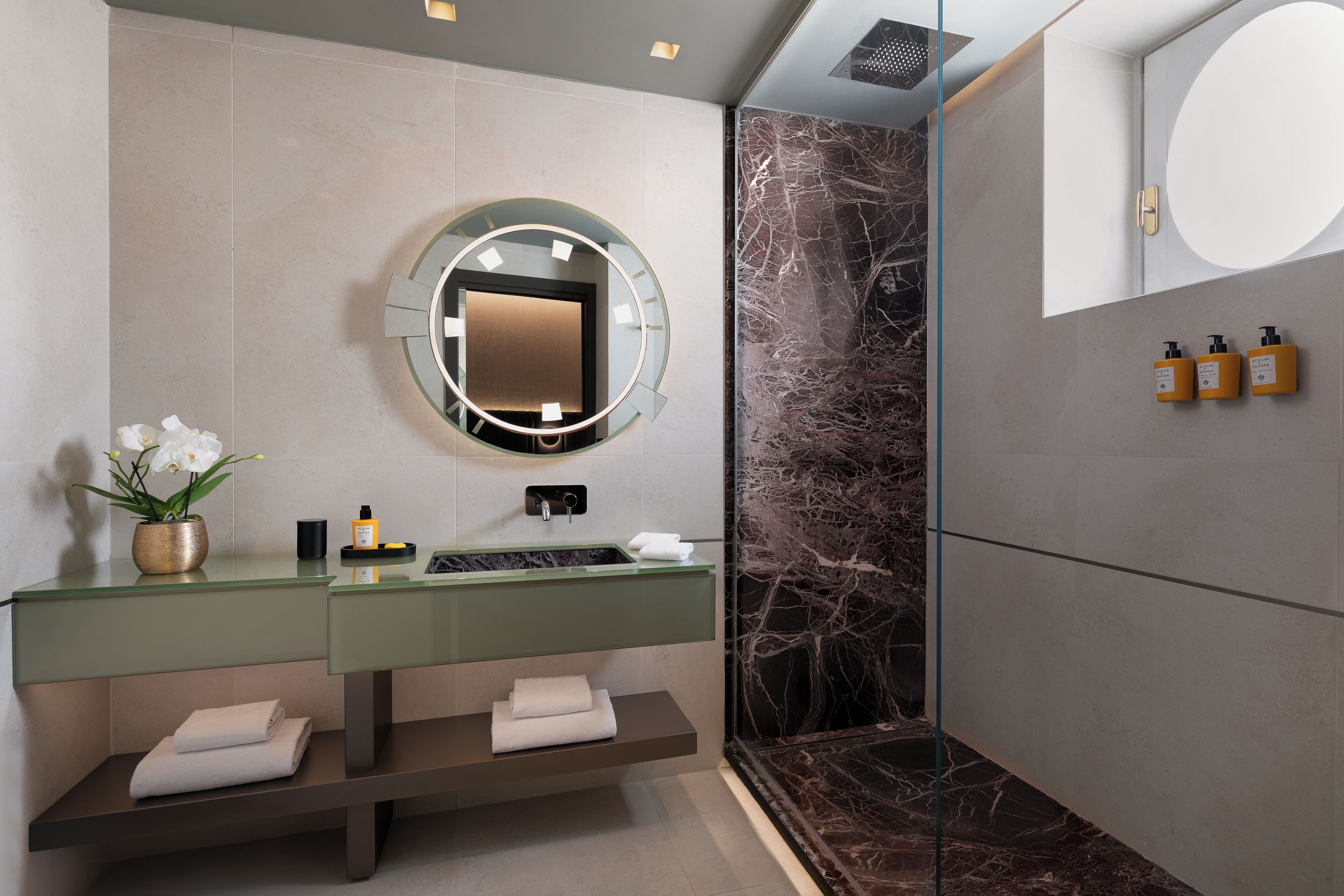 A modern bathroom with a marble wall, a round mirror, and a dual sink vanity.
