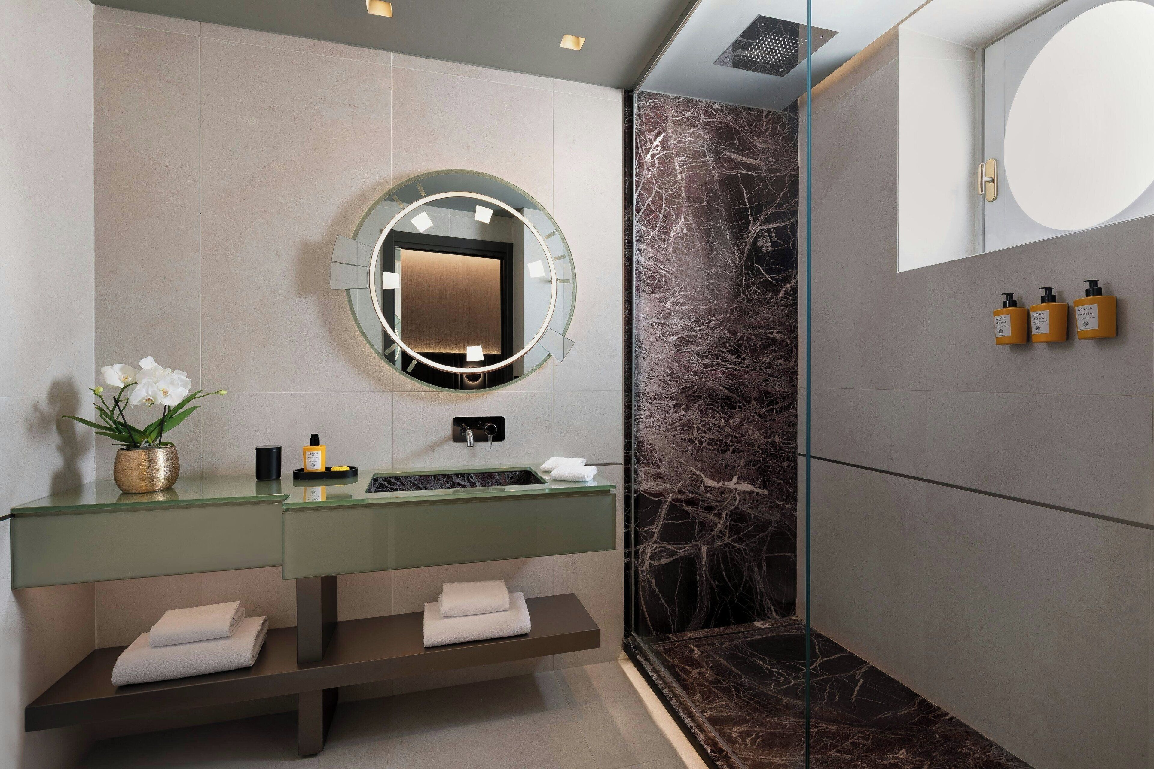 A modern bathroom with a marble shower, a round mirror, and a vanity with a green countertop.