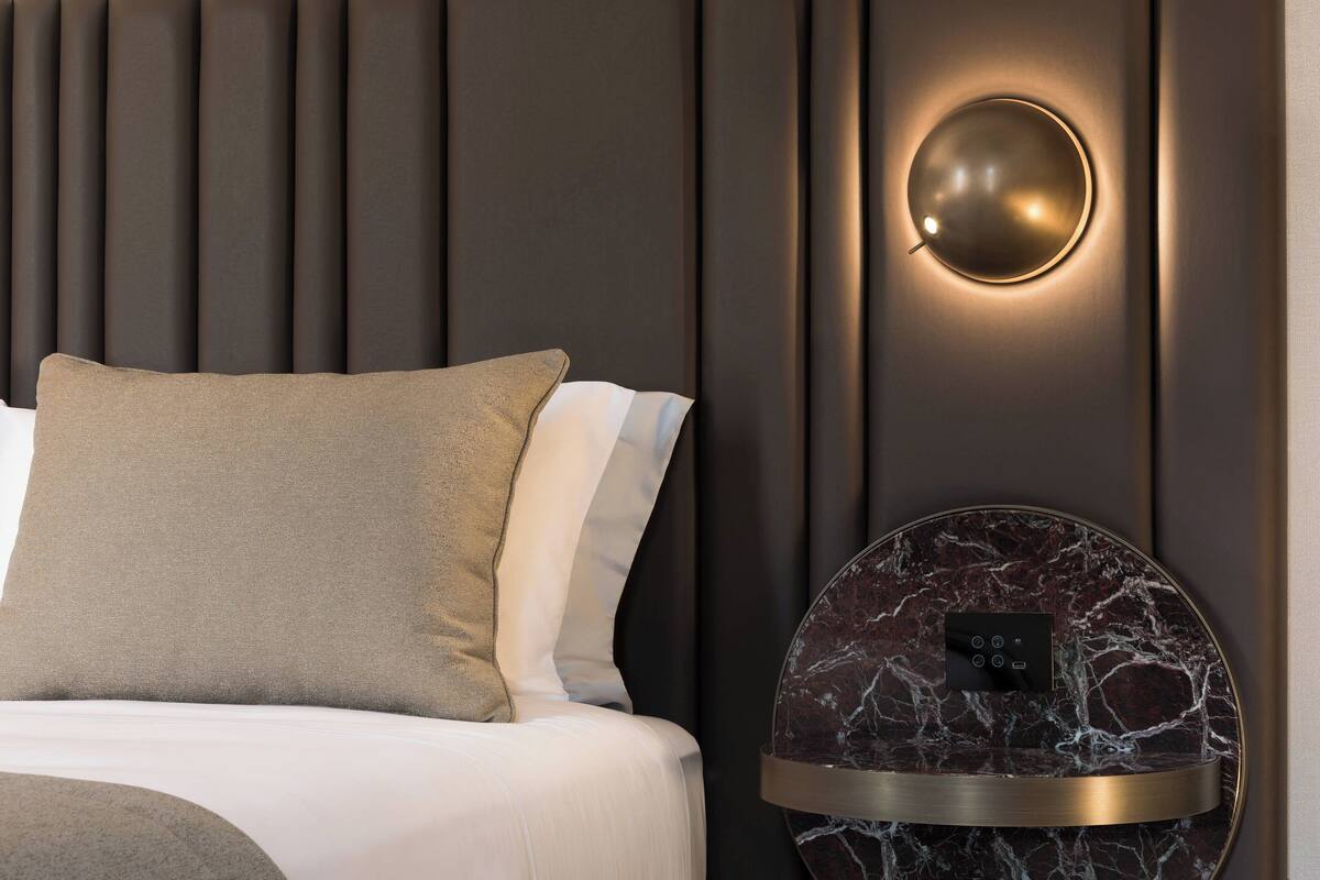 Et moderne hotelværelse med en seng, en rund væglampe og en marmormønstret dekoration på væggen.
