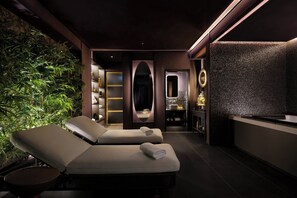A spa room with two reclining chairs, a wall of green plants, a mirror, and a small vanity area.