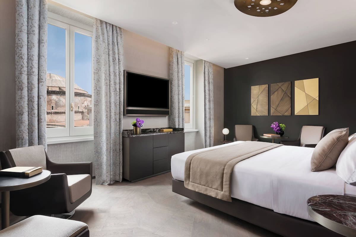 Et moderne hotelværelse med en stor seng, et fjernsyn ophængt på væggen, et skrivebord med stol og udsigt til en bygning.