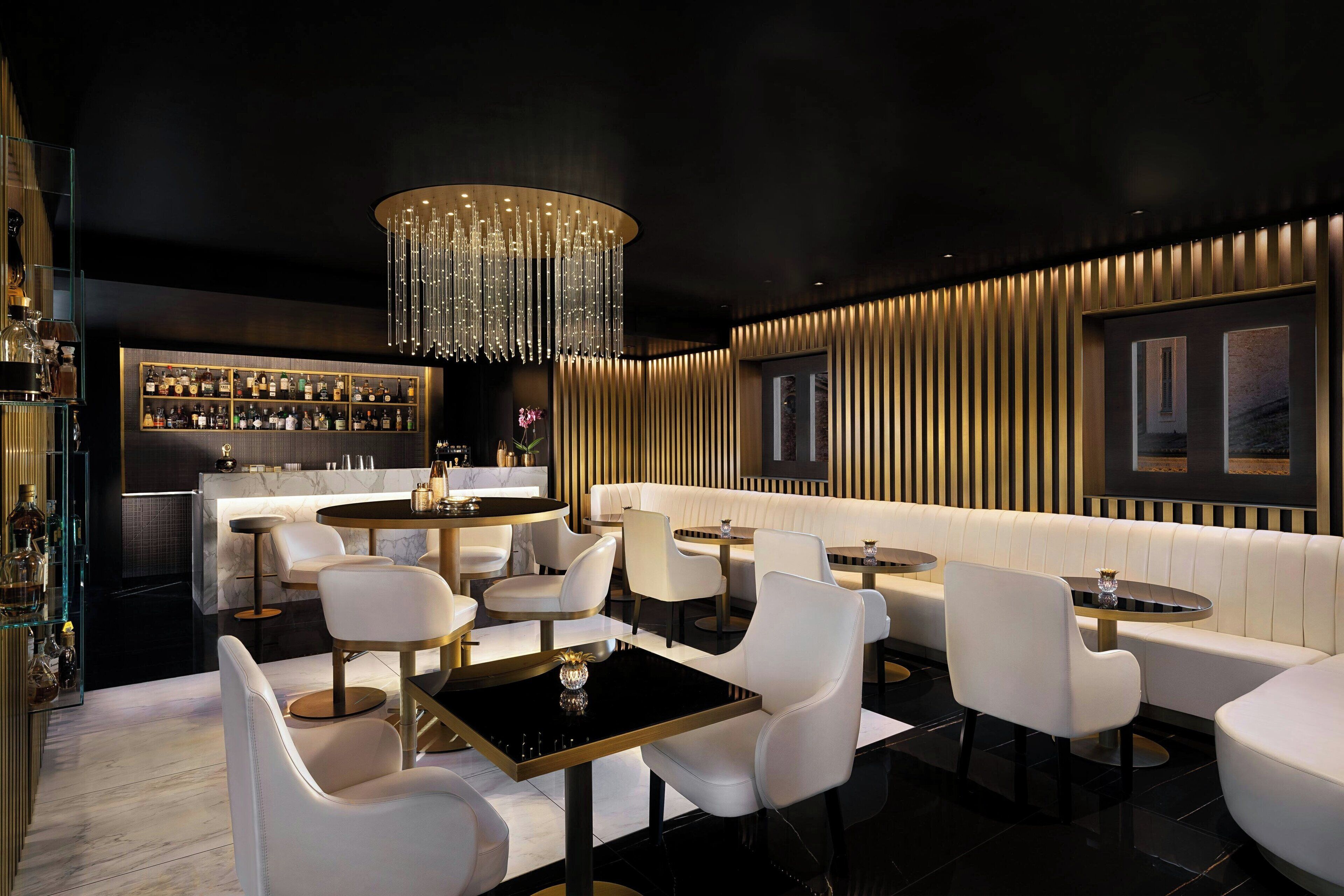 A modern bar area with a bar counter, seating, and a chandelier.