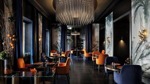Un restaurante moderno con mesas redondas, sillas naranjas y una lámpara de araña en el centro.