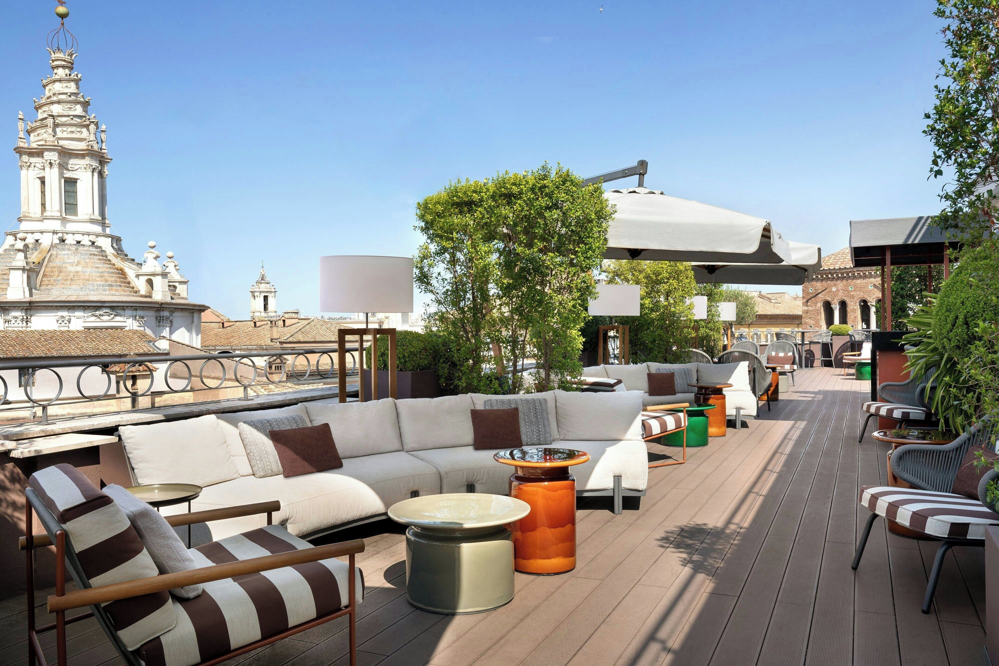 A rooftop terrace with a modern outdoor seating area, including sofas and chairs, and a view of a historic building in the background.