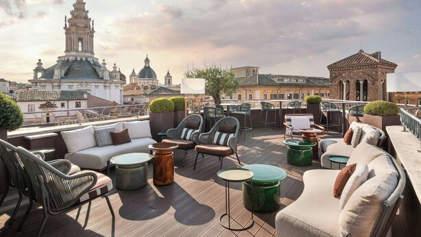 Una terraza en la azotea con mobiliario exterior, incluyendo sofás y sillones, y vistas a edificios históricos al fondo.