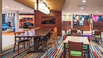 A modern hotel lobby with a large wooden reception desk, seating area with tables and chairs, a stone accent wall, and a colorful mural.
