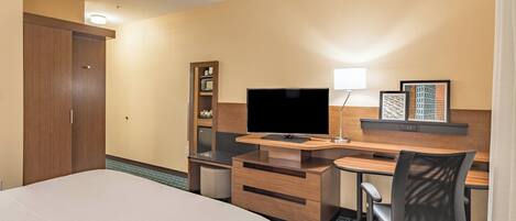 Een hotelkamer met een bed, een bureau met een computer, een stoel, een televisie, een plank met boeken en een kledingkast.