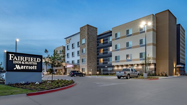 Ein Hotel Fairfield Inn & Suites Marriott mit modernem Design, mehreren Etagen und einem Parkplatz mit Fahrzeugen.