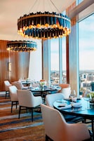 A dining area with round tables, white chairs, and a city view.