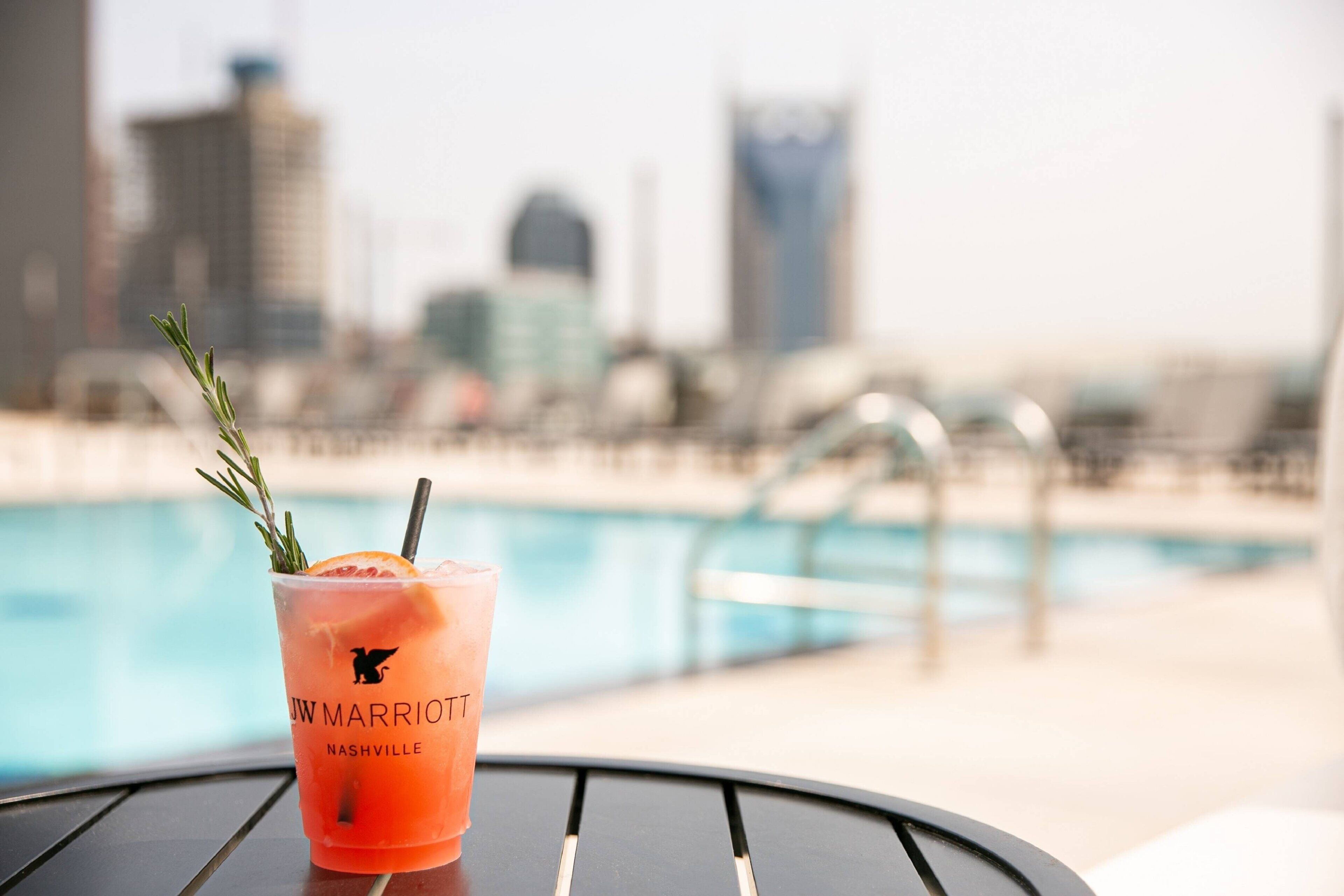 A cocktail with a garnish on a table near a pool, with a city skyline in the background.