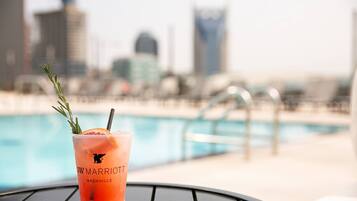 A cocktail with a garnish on a table near a pool, with a city skyline in the background.