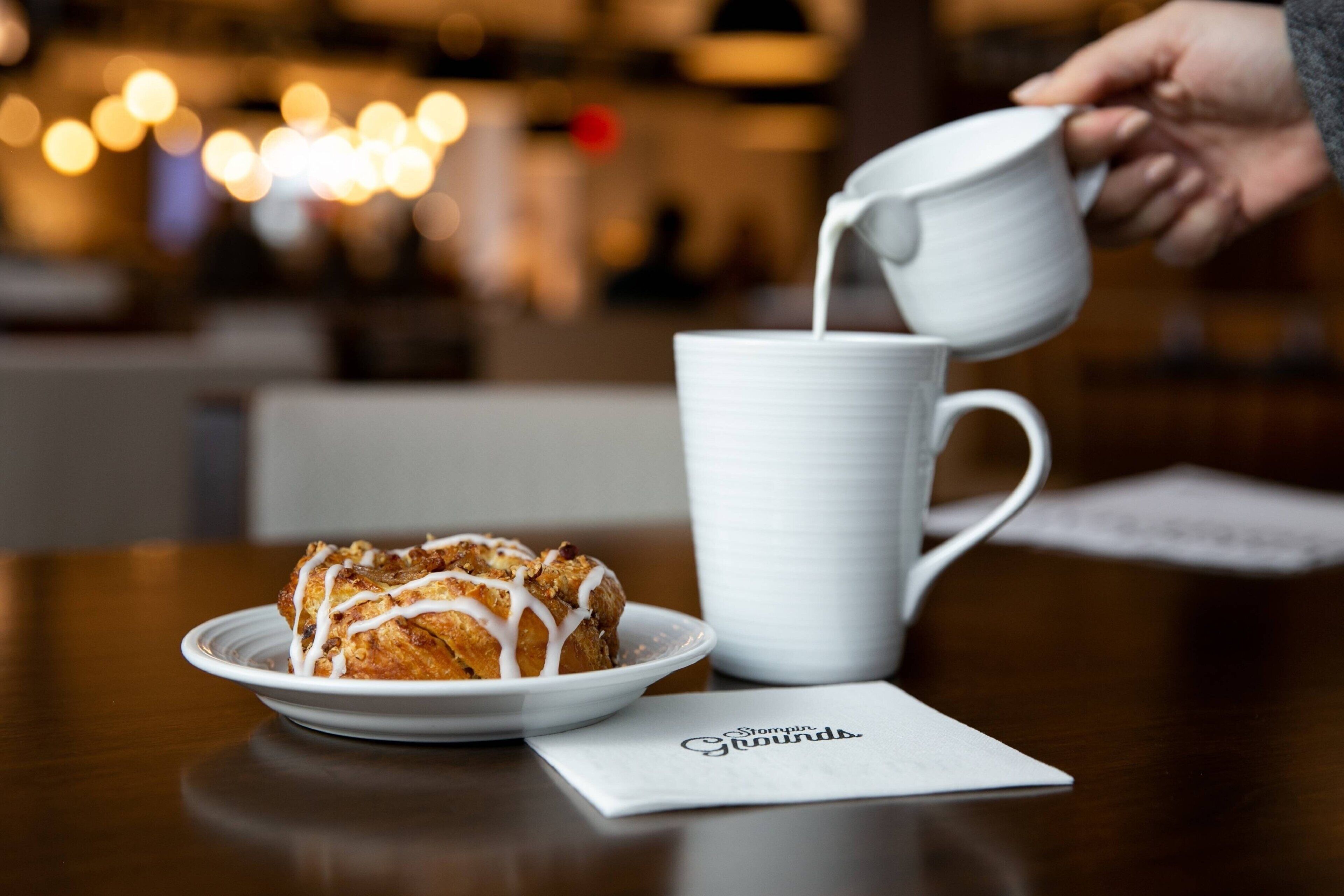 A white ceramic mug on a table with a plate of food beside it.