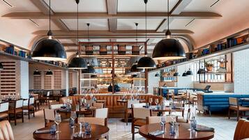 A spacious restaurant with leather booths, round tables, and hanging pendant lights.