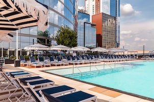 A rooftop pool area with lounge chairs and umbrellas, surrounded by modern buildings.