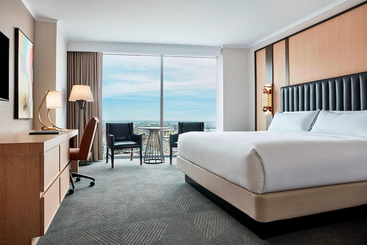 Une chambre d’hôtel avec un grand lit, un bureau avec une chaise, une petite table et une vue sur la ville grâce à de grandes fenêtres.