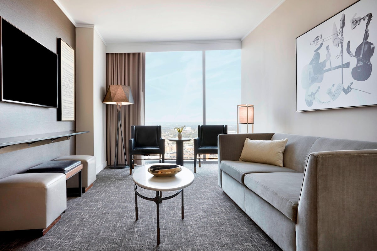 Une chambre d’hôtel moderne dotée d’une grande fenêtre, d’un téléviseur à écran plat, d’un canapé, d’une table basse et d’un tableau représentant des instruments de musique.