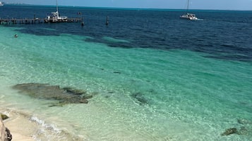 Een strand met helder turquoise water, een pier en een zeilboot.
