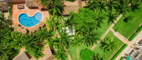 An aerial view of a resort with a heart-shaped pool surrounded by palm trees and a well-maintained lawn.