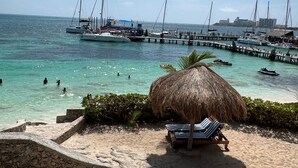 A beach with a thatched umbrella, lounge chairs, and a stone wall. - Dos Playas by Faranda All Inclusive (Cancun)