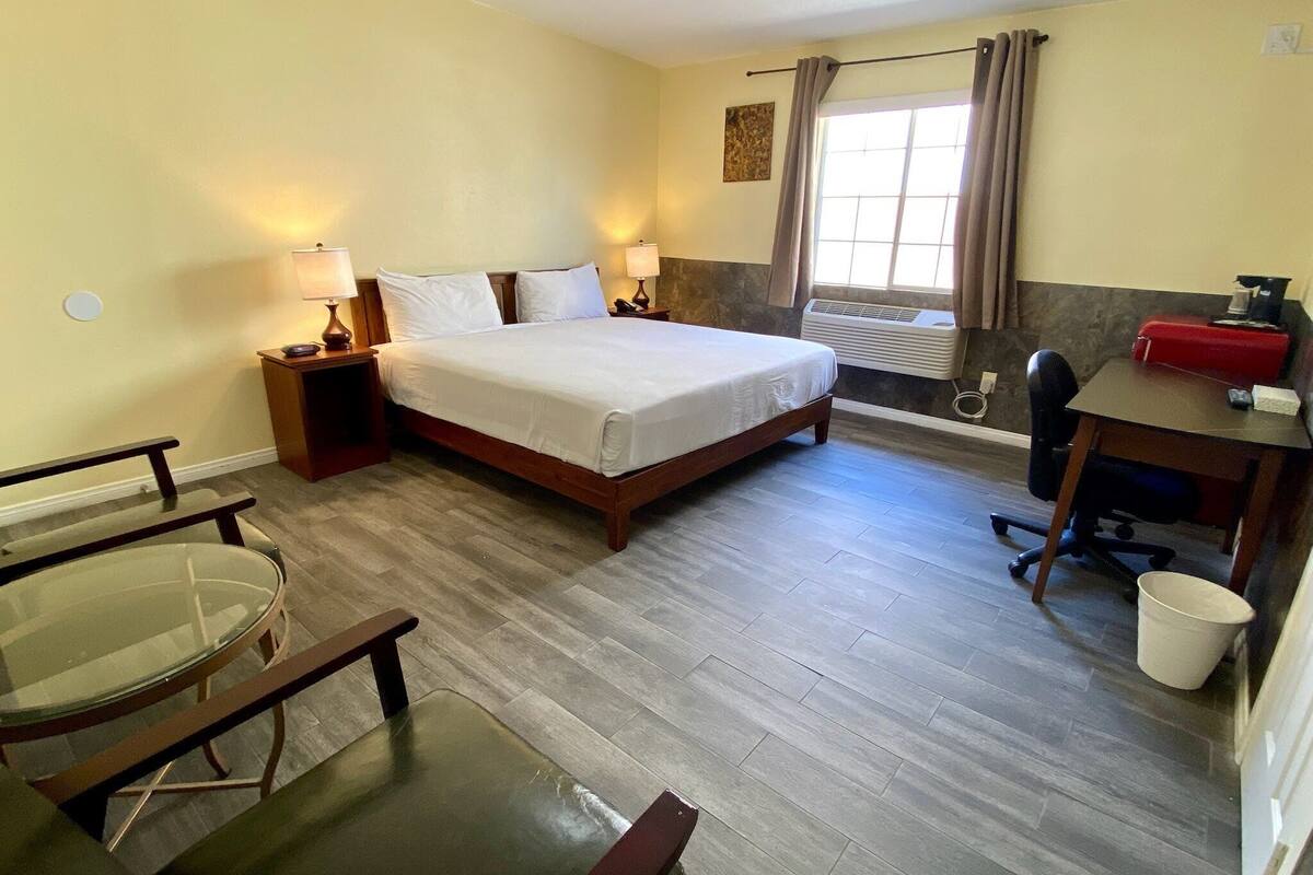 Habitación de hotel con cama, lámparas de noche, escritorio con silla, una mesita y una ventana con cortinas.